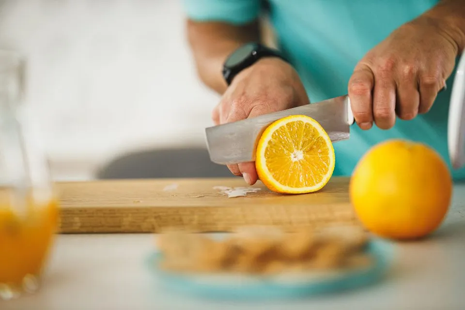 Hands cutting an orange, with a glass of juice beside them